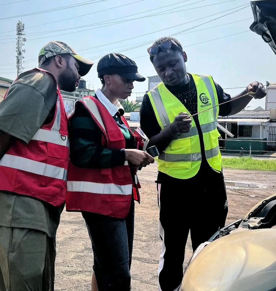 An instructor drawing the oil dipstick while two students watch over the open bonnet