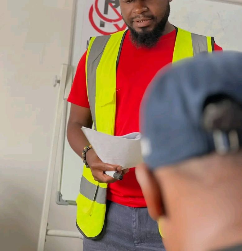 An instructor reading from a sheet in the classroom, a chart of road signs on the whiteboard behind him